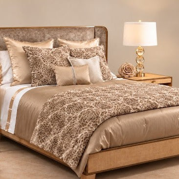 A luxury bed dressed in Judith Leiber Couture x Ann Gish Monaco Crystal and Astera bedding, featuring beige and gold embroidered floral pillows, solid beige bedding, a coordinating floral throw blanket, multiple decorative pillows, an upholstered headboard, and a gold bedside lamp on a wooden nightstand. - THAAK-GPU PWAA2424-GPU COMOK-MYS-PUM
COMOQ-MYS-PUM