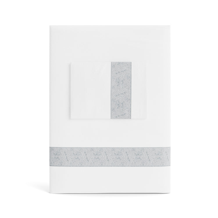 A folded white Minaudiere Sheet Set by Judith Leiber Couture x Ann Gish, shown with its matching pillowcase on top, featuring a silver sequenced border band that mirrors the jeweled sparkle of the Minaudiere design. - SSMIK-WHI-SIL SSMIQ-WHI-SIL