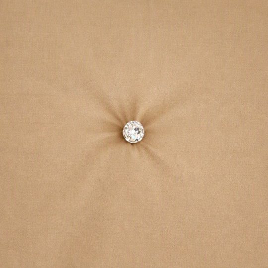 A single round clear crystal or gemstone stud with a silver-toned setting, centered on a soft, sandy beige fabric background. Swatch of Monaco Crystal in Sand - COMOK-SAN-IVO COMOQ-SAN-IVO THMOK-SAN-IVO