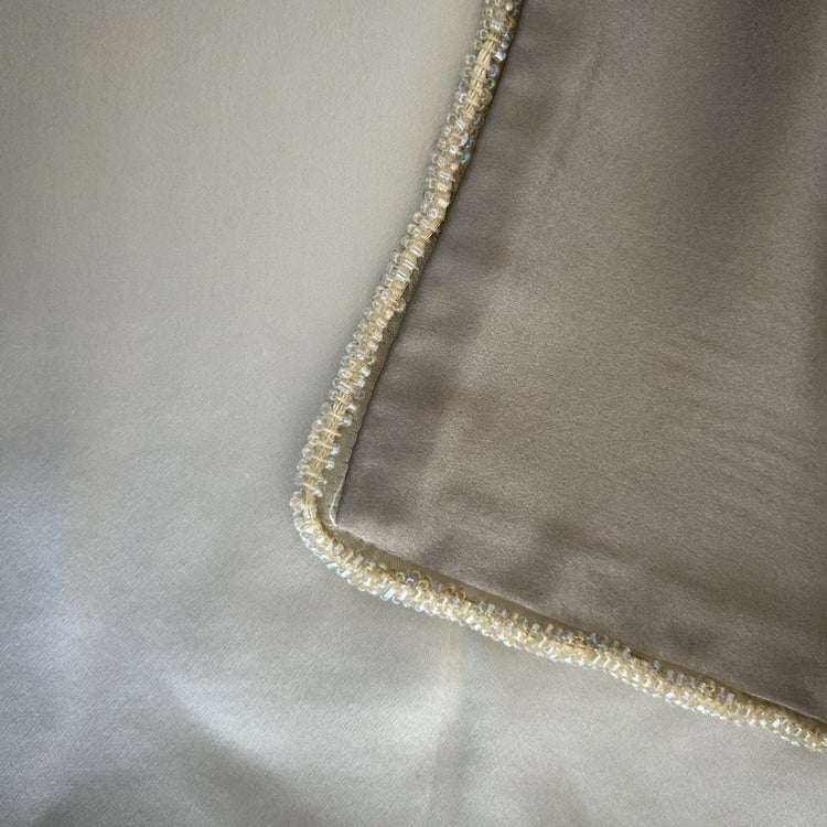 Close-up of a metallic silk fabric corner with a decorative border of small iridescent pearls and clear rhinestones on top of silver silk fabric. - SHMOE-MET-SIL SHMOK-MET-SIL SHMOS-MET-SIL PWMO3616-MET-SIL